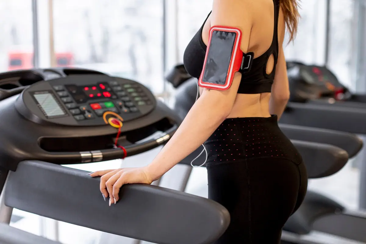 A fitness enthusiast using a wearable heart rate monitor and a gym mobile app to track workout data, representing modern digital integration in top-tier fitness facilities.