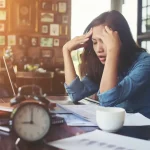 Woman sitiing her office putting her hands on her head facing stress.