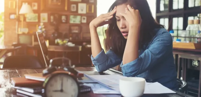 Woman sitiing her office putting her hands on her head facing stress.
