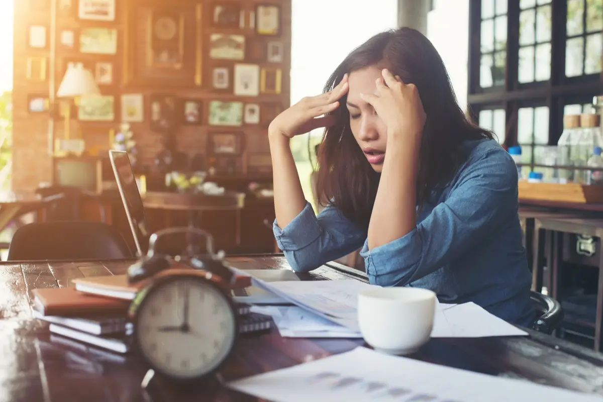 Woman sitiing her office putting her hands on her head facing stress.