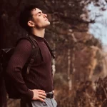 Person standing outdoors practicing stress management breathing techniques in natural light