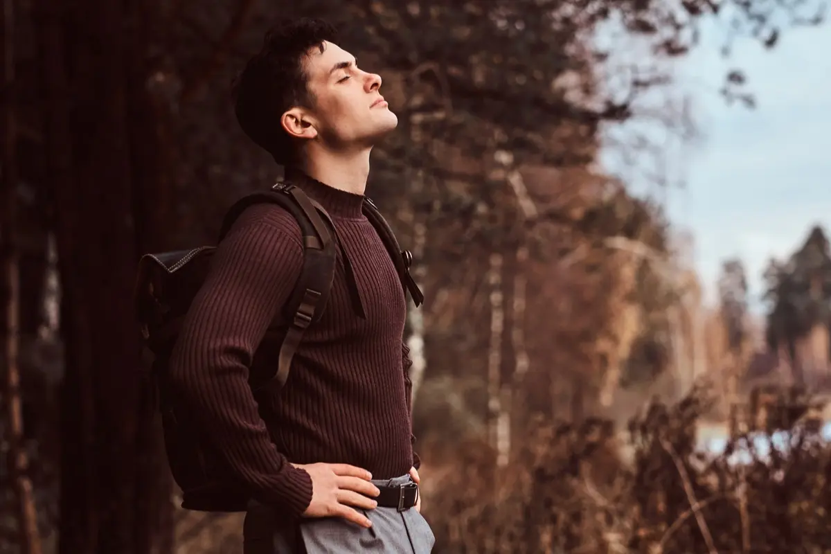 Person standing outdoors practicing stress management breathing techniques in natural light